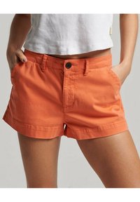 Pomarańczowe bawełniane szorty z płaskim przodem, dwoma bocznymi kieszeniami i zapięciem na guzik. Posiadają podwinięty dół oraz gładką fakturę.