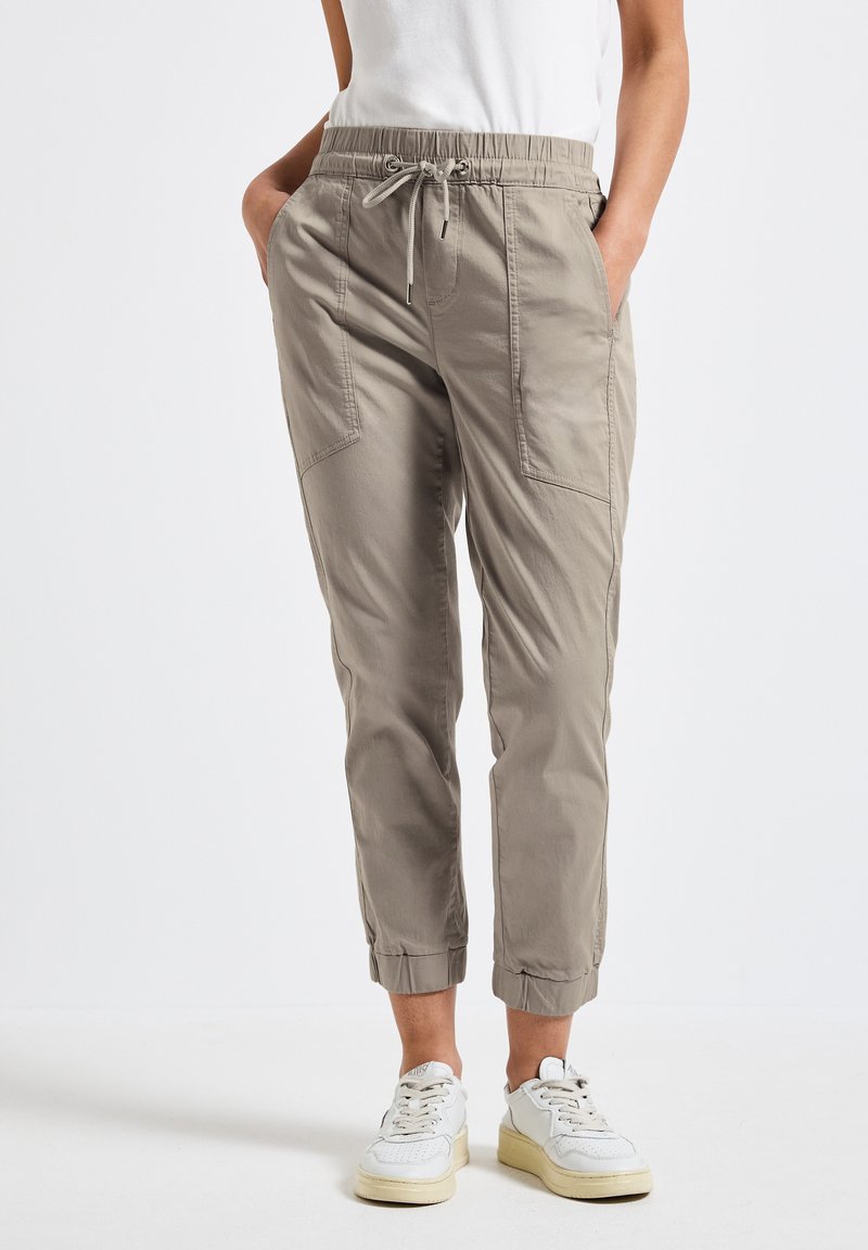 Pantalons de jogging légers de couleur brun clair, avec une taille élastique, un cordon de serrage et des poches latérales. Chevilles resserrées et texture de tissu lisse.