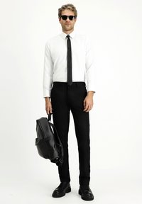 Outfit formale composto da una camicia bianca a maniche lunghe, cravatta nera, pantaloni neri su misura e scarpe di pelle nere, con uno zaino in pelle nera.