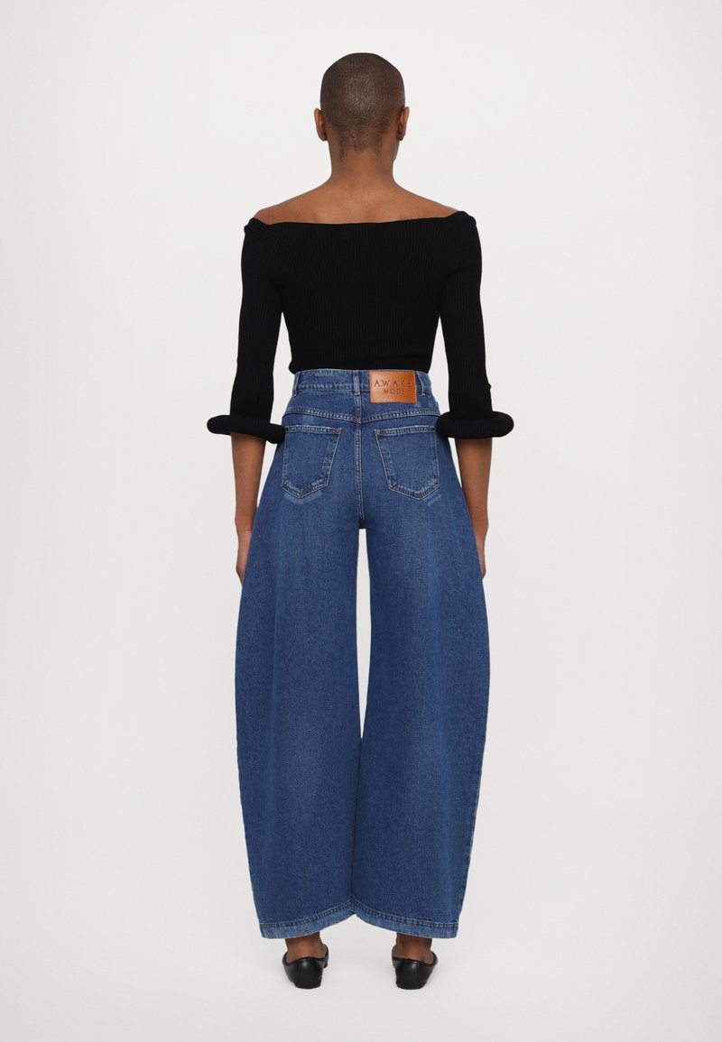 Top off-shoulder a coste nera e jeans in denim blu a gamba larga con etichetta in pelle sulla vita posteriore, senza motivi visibili, texture liscia.