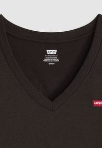 Schwarzes V-Ausschnitt-T-Shirt aus Baumwolle mit einem roten Levi's-Logo-Tag. Der Stoff ist glatt und hat eine klassische Passform. Pflegeetikett sichtbar im Halsbereich.