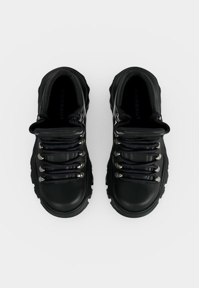 Ζευγάρι μαύρα δερμάτινα ορειβατικά μποτάκια με χοντρές σόλες και μεταλλικά κουμπώματα, από πάνω σε λευκό φόντο.