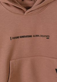 Sweat à capuche marron avec un texte noir "FUTURE GENERATIONS GLOBAL CREATIVES" au-dessus de la poche avant.
