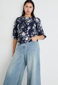 Top floreale navy con motivi bianchi, maniche a sbuffo e scollatura rotonda, abbinato a jeans larghi di colore azzurro realizzati in denim.