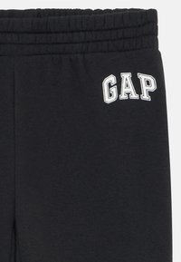 Melnas sporta bikses, izgatavotas no kokvilnas maisījuma auduma. Satur elastīgu jostasvīru un balto "GAP" logo izšūtu kreisajā pusē.