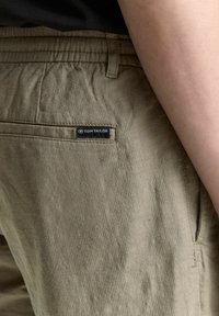 Khaki bikses, izgatavotas no viegla auduma, ar elastīgu jostu un aizmugurējo kabatu ar redzamu "TOM TAILOR" logo birku.