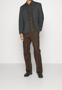 Grå blazer med strukturerade axlar, brun skjorta med knappar, bruna byxor och svarta loafers med texturerad detalj.