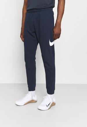 Nachtblaues Sweatpants mit einem weißen Nike-Logo auf dem linken Oberschenkel, elastischem Taillenbund und Bündchen. Kombiniert mit weißen Sportschuhen.