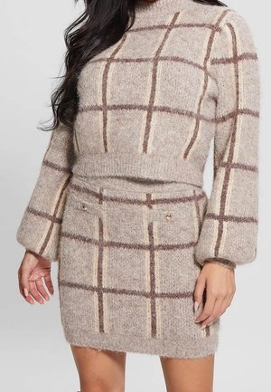 Mujer con vestido de punto beige y textura peluda, con patrón de cuadricula marrón, mangas largas abullonadas y bolsillos con botones en la falda.