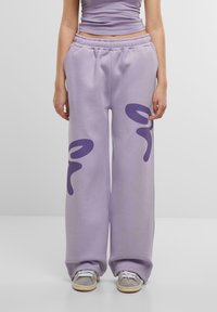 Lila sweatpants med elastisk midja, som har stora abstrakta lila mönster framtill och en avslappnad passform ner till anklarna.