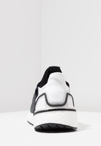 Czarno-biały but sportowy z teksturowaną górą z tkaniny, grubą białą podeszwą środkową o teksturowanym wzorze oraz elastyczną czarną podeszwą.