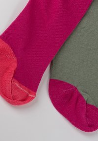 Un paio di calze con una parte superiore rosa e corallo e un corpo verde. Il materiale è a coste e presenta una costruzione senza cuciture per la punta.