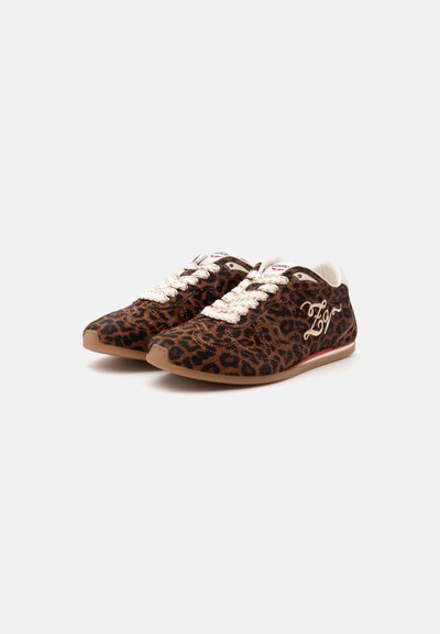 Paire de baskets basses avec imprimé léopard marron et noir, lacets blancs et texte blanc brodé sur le côté.