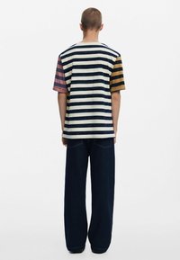 Striped t-shirt with varying colors: dark blue, beige, pink, and yellow. Loose design paired with dark wide-leg jeans. Minimalistic styling.