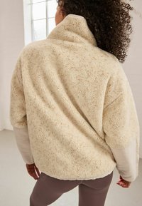 Cremefarbener Fleece-Pullover mit hohem Kragen, weicher Textur und lässiger Passform. Funktionen lange Ärmel und eine unauffällige Nahtdetails.