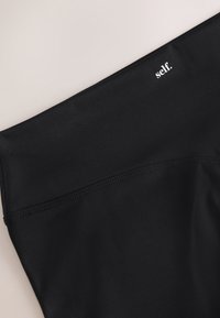 Leggings atletici neri a vita alta, realizzati in tessuto liscio ed elastico. Presentano un logo discreto e un dettaglio con cuciture sulla cintura.