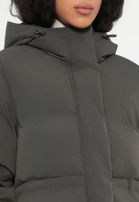 Mujer con una chaqueta de invierno acolchada de color gris oscuro con un alto cuello y cuerdas ajustables en la capucha.