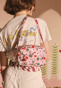 Rosa blomster crossbody taske med et tekstureret mønster, gyldent hardware, lynlåslommer og dekorative kirsebær charms. Justerbar rem.
