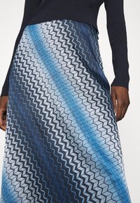 Närbild av en person som bär en marinblå topp och en kjol med blått zickzack-mönster och diagonala ränder i varierande nyanser av blått.