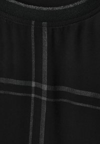 Svart tygtop med en subtil grå rutmönster, ribbad halsringning och en mjuk textur. Fokusera på eleganta designelement.