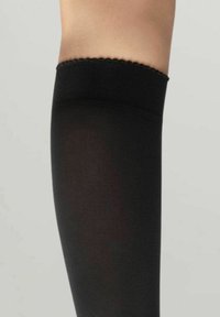 Schwarze Oberschenkelstrümpfe mit glatter Oberfläche und einem gezackten Spitzenabschluss, entworfen für Komfort und eine enge Passform.