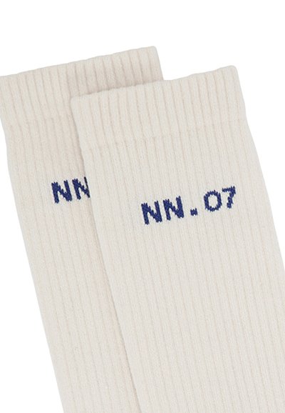 Calze a coste beige con ricamo blu scuro "NN.07" vicino alla parte superiore. Realizzate in un tessuto morbido ed elastico per garantire comfort e vestibilità.