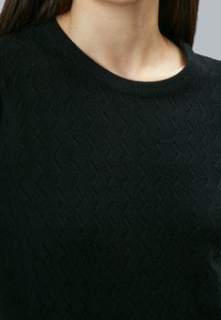 Schwarzer Strickpullover mit strukturiertem Zickzackmuster, Rundhalsausschnitt und geripptem Saum am Kragen, aus weichem Stoff gefertigt.