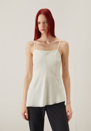 Lys ivor camisole med tynne skulderstropper, kvadratisk utringning, flytende form og jevn tekstur. Kombinert med mørke bukser.