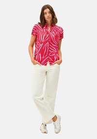 Camicetta rosa a maniche corte con motivo botanico bianco, abbinata a pantaloni bianchi a gamba larga e sneakers. Vestibilità comoda, tessuto traspirante.