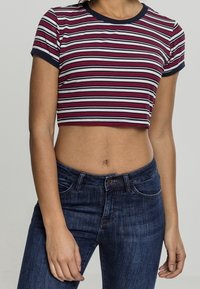 Camiseta recortada de canalé con rayas horizontales en rojo, blanco y azul marino. Presenta un cuello azul marino y mangas cortas. Combinada con jeans de un azul oscuro.