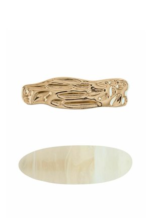 Zwei Haarspangen auf weißem Hintergrund, eine unregelmäßig strukturierte goldfarbene Metallspange und eine glatte ovale beige Harzspange.
