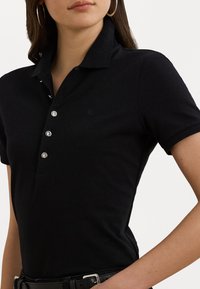 Svart polo-skjorte med krage, med fire sølvknapper, teksturert stoff og en liten preget logo på brystet.