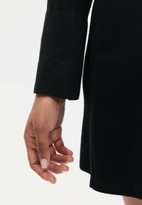 Czarny sweter dzianinowy z prążkowanymi mankietami, z haftowanym detalem w kształcie litery "B" na rękawie. Gładka tekstura i dopasowany krój.