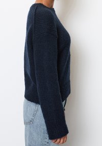 Navyblauer Strickpullover mit langen Ärmeln, strukturiertem Stoff, verkürztem Design und geripptem Saum, kombiniert mit hellblauer Jeans.