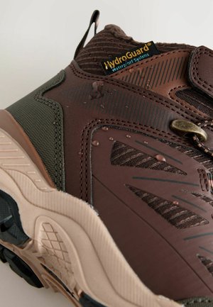 Bordeauxkleurige waterdichte wandelschoen met een gestructureerd oppervlak, een rubberen buitenzool en een mesh voering. Voorzien van zwarte en bordeauxkleurige accenten, waaronder banden.