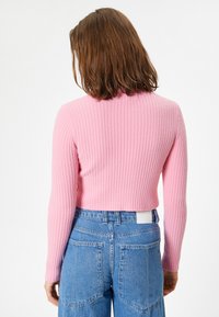 Maglione corto a coste in morbido cotone rosa, con maniche lunghe. Abbinato a jeans in denim blu a vita alta con tasche a toppa.