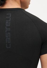 Schwarzes Sportshirt mit strukturierter Stoffoberfläche, kurzen Ärmeln und einem Logo in einer dunkleren Schwarztönung auf dem Rücken.