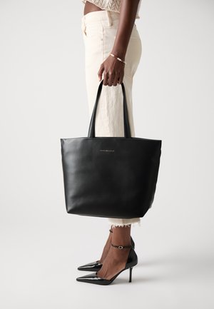 Zwarte leren tote bag met een gladde textuur, rechthoekige vorm en twee lange handvatten; voorzien van een minimalistisch gouden logo detail aan de voorkant.