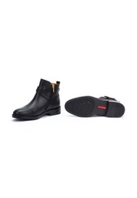 Bottines en cuir noir avec fermeture éclair, talon plat, semelle texturée et couleur intérieure contrastante, dotées d'une sangle décorative.