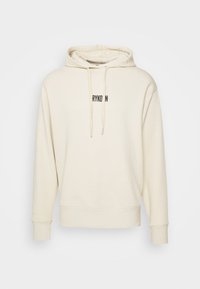 Kremowa bluza z kapturem wykonana z miękkiego materiału, wyposażona w kaptur, ściągacze i czarne logo z przodu. Ściągacze na mankietach i w pasie.