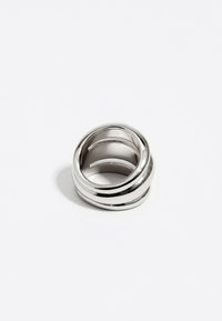 Anillo de metal plateado con un acabado suave y pulido; presenta tres bandas circulares entrelazadas, creando un diseño abierto y en capas.