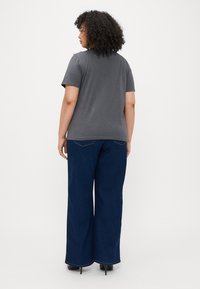 Grå t-skjorte med korte ermer, kombinert med vide mørkeblå jeans. Glatt stoff med et enkelt design. Skoene er svarte med hæl.