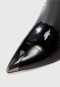 Black patent leather ankle boot with a pointed toe, featuring a metallic accent at the toe and a smooth, shiny texture.