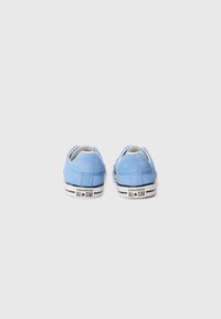 Baskets Converse All Star en suede bleu clair avec un design bas, dotées de semelles en caoutchouc rayées noires et blanches et d'un logo sur le talon.