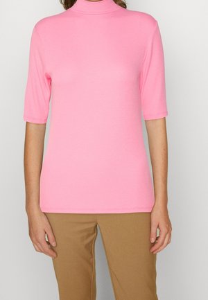T-shirt rose côtelé avec un col montant et des manches courtes, présentant une coupe près du corps et une texture lisse. Porté avec un pantalon beige.