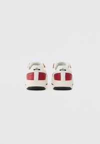Hvite og røde lær-sneakers med lavt design, som har en hvit hælflik og svart gummisåle. Enkelt merke detaljer nær hælen.