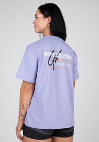 Lilac short-sleeve t-shirt featuring bold "GORILLA WEAR" branding on the back, vibrant graphics, and a relaxed fit.