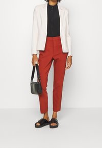 Blazer blanc, chemise noire à boutons, pantalon rouge cintré, sac à main noir et sandales à glisser noires. Tissu lisse, design structuré.