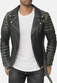 Giacca da motociclista in pelle nera e verde con design trapuntato sulle spalle, cerniere asimmetriche e bottoni a pressione. Finitura texture con fibbia regolabile.