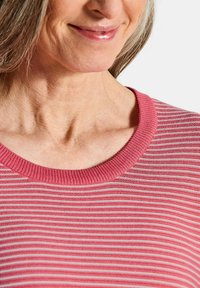 Gestreifter, rosa und weißer Strickpullover mit einem gerippten Rundhalsausschnitt. Weiche Textur mit sichtbaren Nähdetails entlang des Ausschnitts.